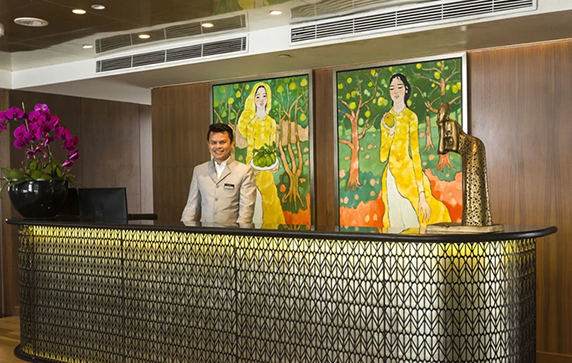 A staff member standing behind the reception desk on board the Scenic Spirit cruise ship. 