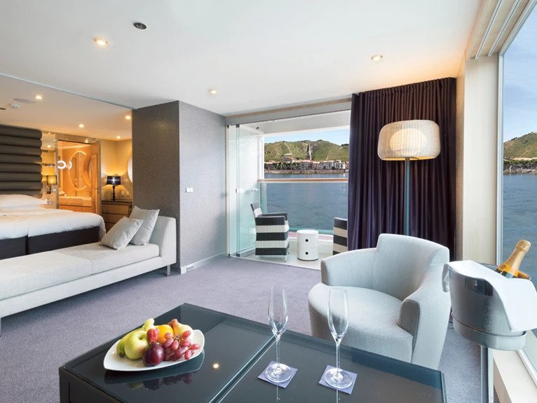 The  Royal Suite with seating areas and a bed, with floor-to-ceiling windows that provide views of the river outside