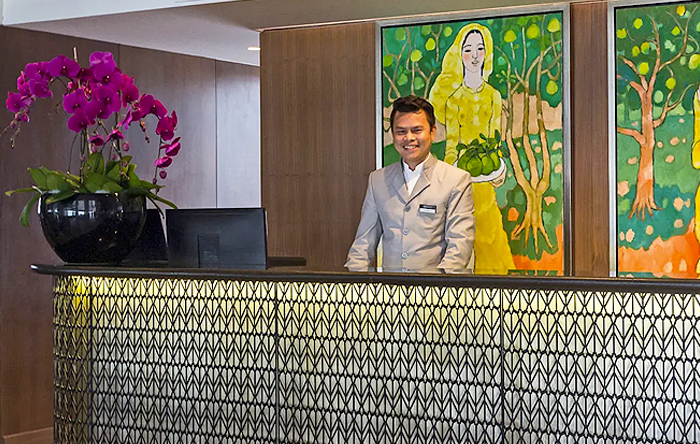 A smiling staff member standing behind the welcoming reception desk on board the Scenic Spirit ship.