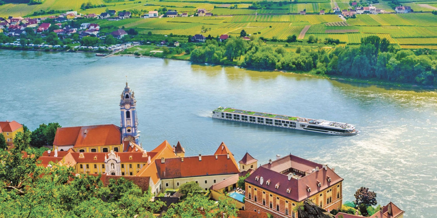 A Scenic cruise ship gliding along the Danube River, surrounded by green fields and historical architecture in Durnstein, Austria.