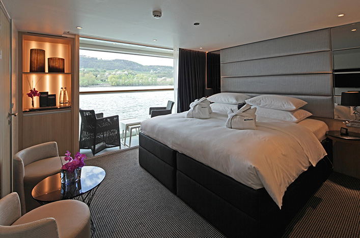 Comfortable queen bed and views of the passing river from the Scenic Sun Lounge area in a Junior Suite.