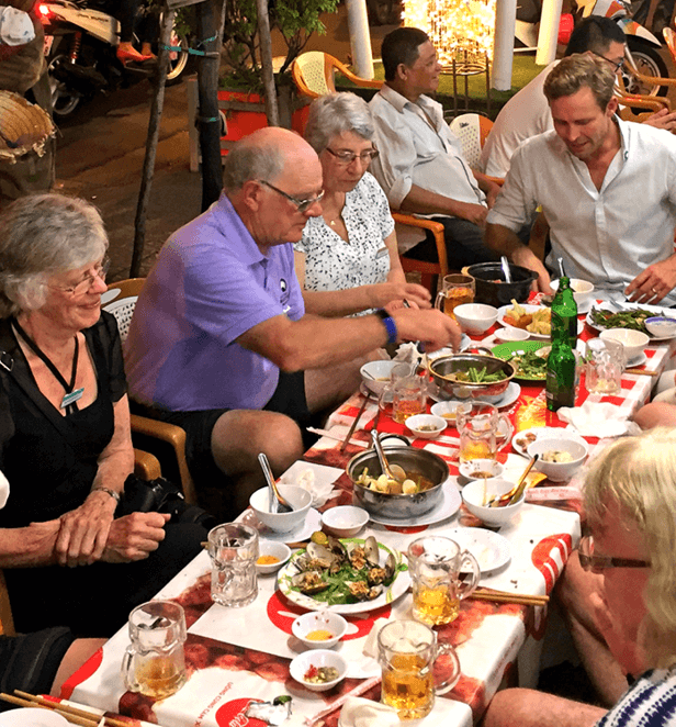 Group of people dining together at a Vietnamese street food restaurant with various dishes and beer.