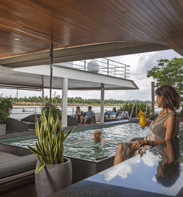 Woman relaxing with a drink beside the pool on board Scenic Spirit, overlooking the river scenery in Southeast Asia.
