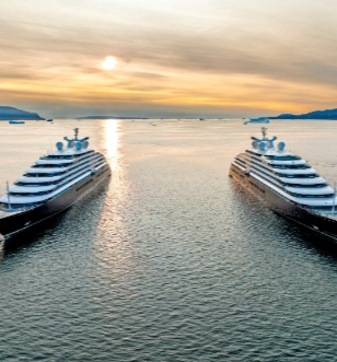 Scenic Eclipse and Scenic Eclipse II sail through Disko Bay, silhouetted against a vibrant sunset sky.